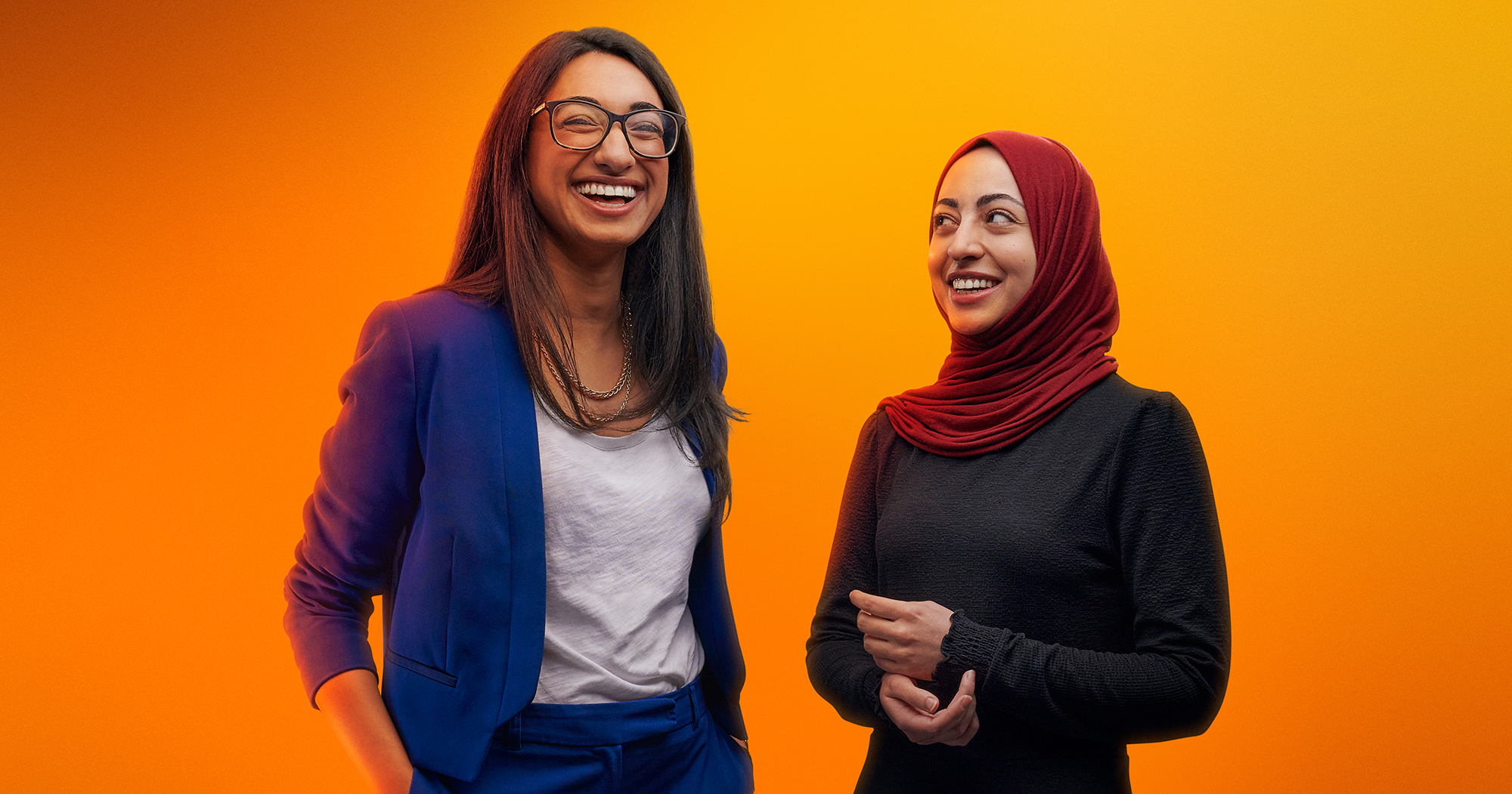 2 Frauen stehend lachend vor orangenem Hintergrund